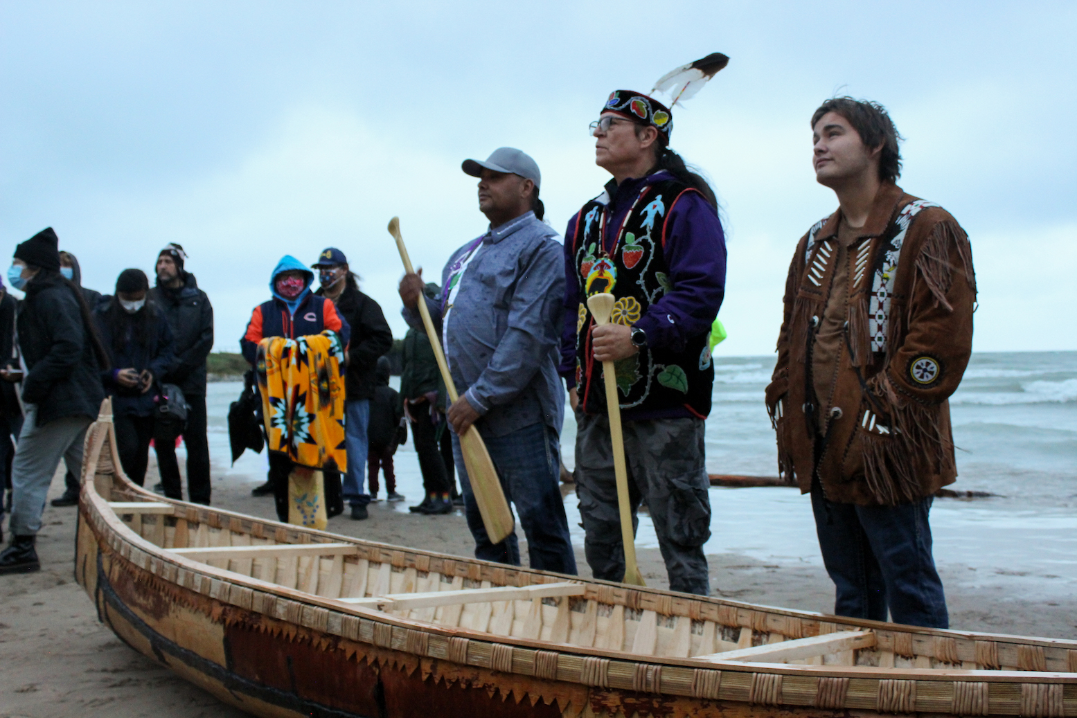 Apprentices and Valliere stand with the completed canoe in front of Lake Michigan.                