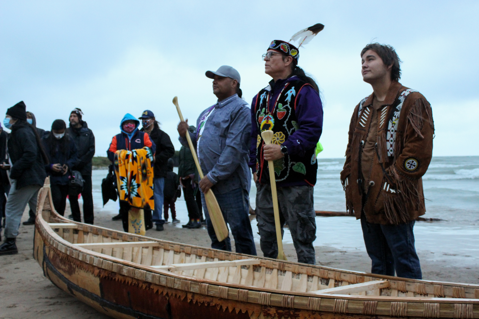 Apprentices and Valliere stand with the completed canoe in front of Lake Michigan.