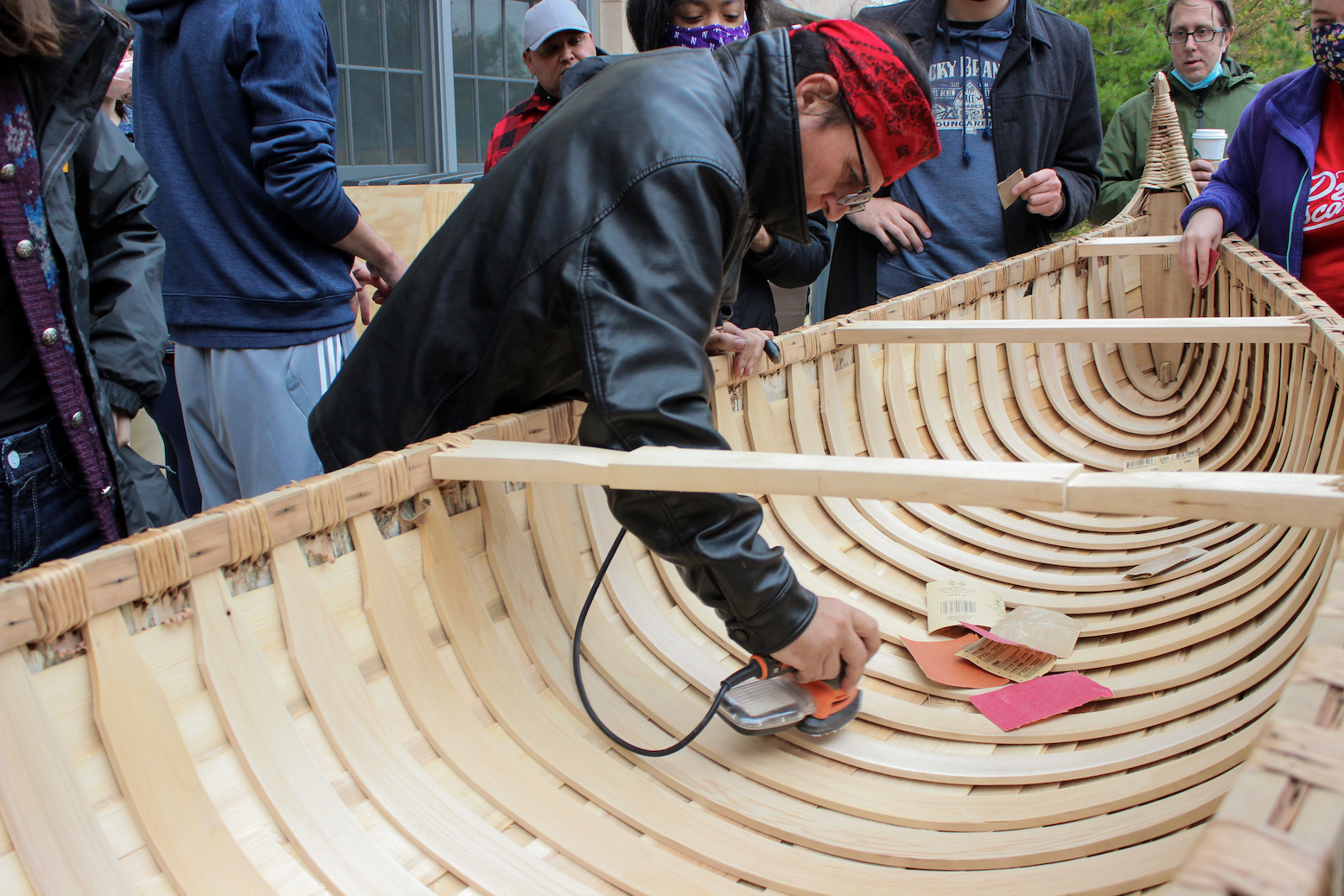 Valliere sands the ribs of the canoe with a power sander.